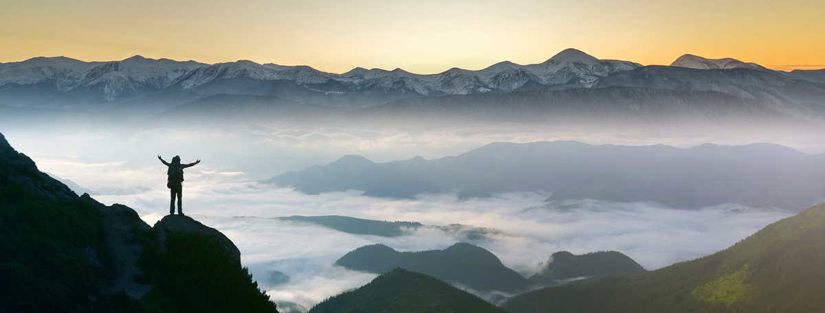 Silhouette of backpacker on rocky mountain slope with raised hands over valley