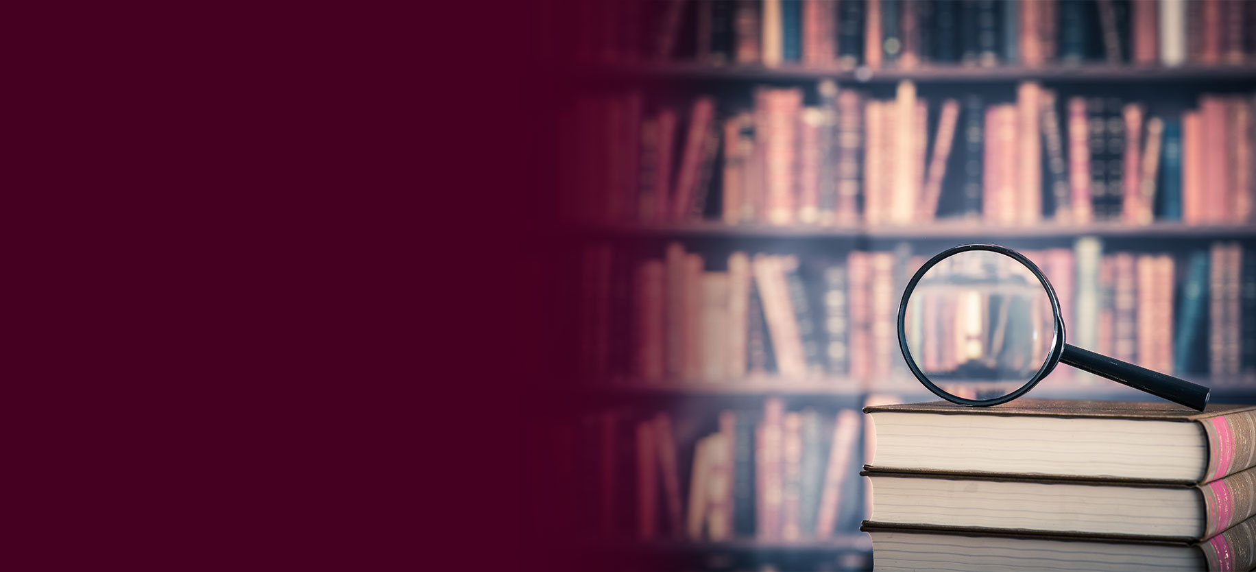 A magnifying glass sits on top of a stack of books in front of a book shelf