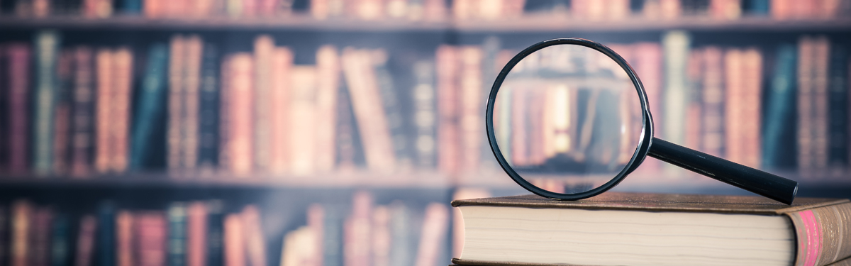 A magnifying glass sits on top of a stack of books in front of a book shelf