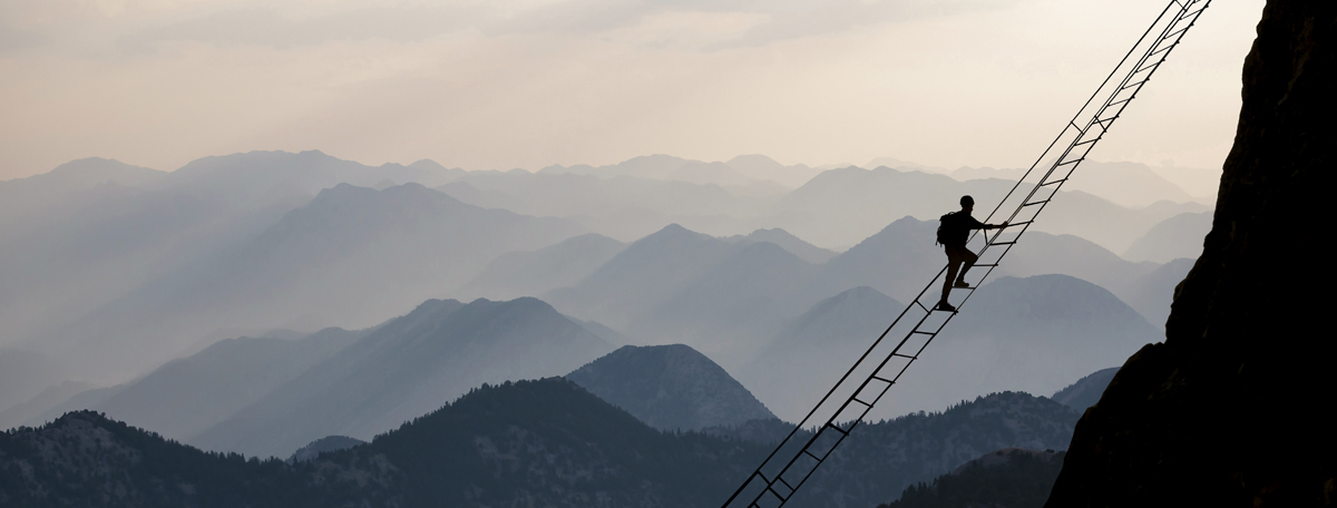 A person climbing a mountain on a rope ladder