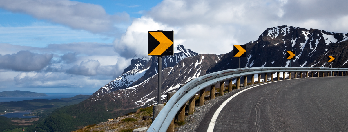 Guardrails on the edge of a curving road with warning signs