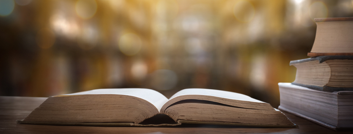 A book lays open on a library table with a stack of books beside it