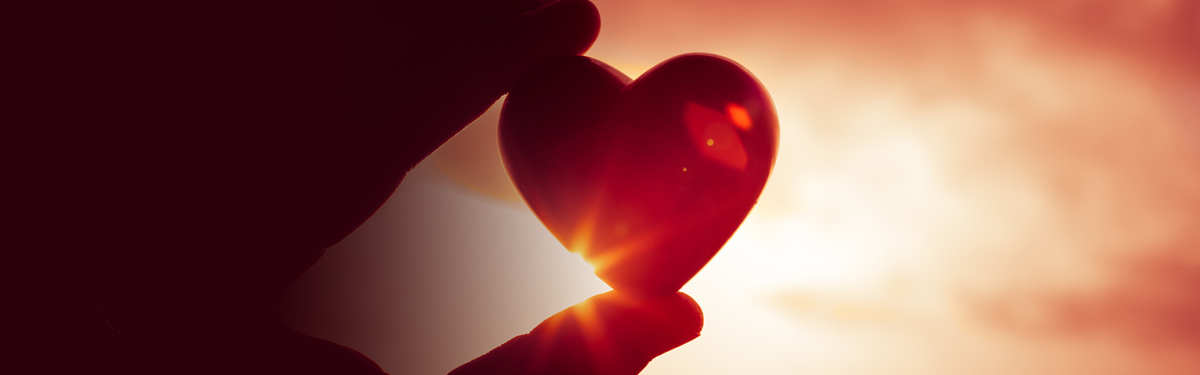 A hand holding a heart shaped object up to the sky